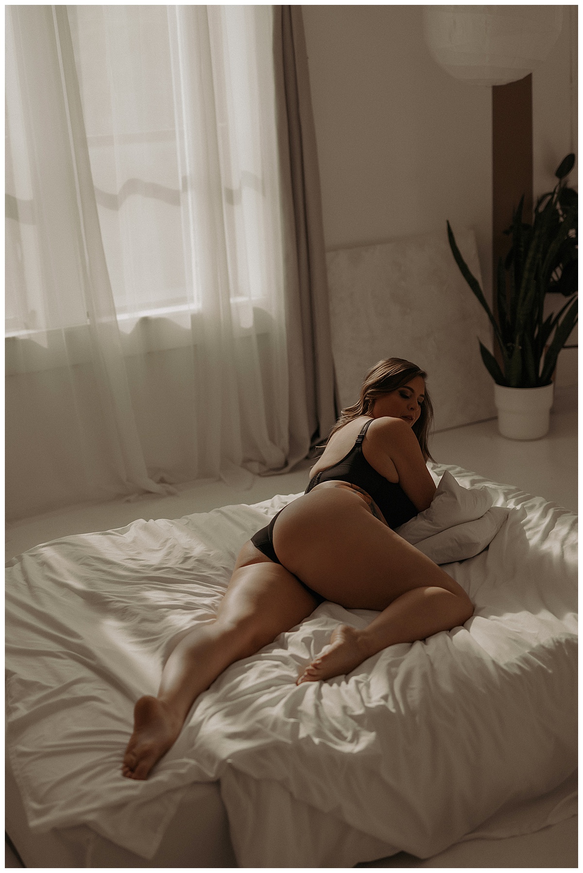 Adult lays on the bed wearing black lingerie for Mary Castillo Photography