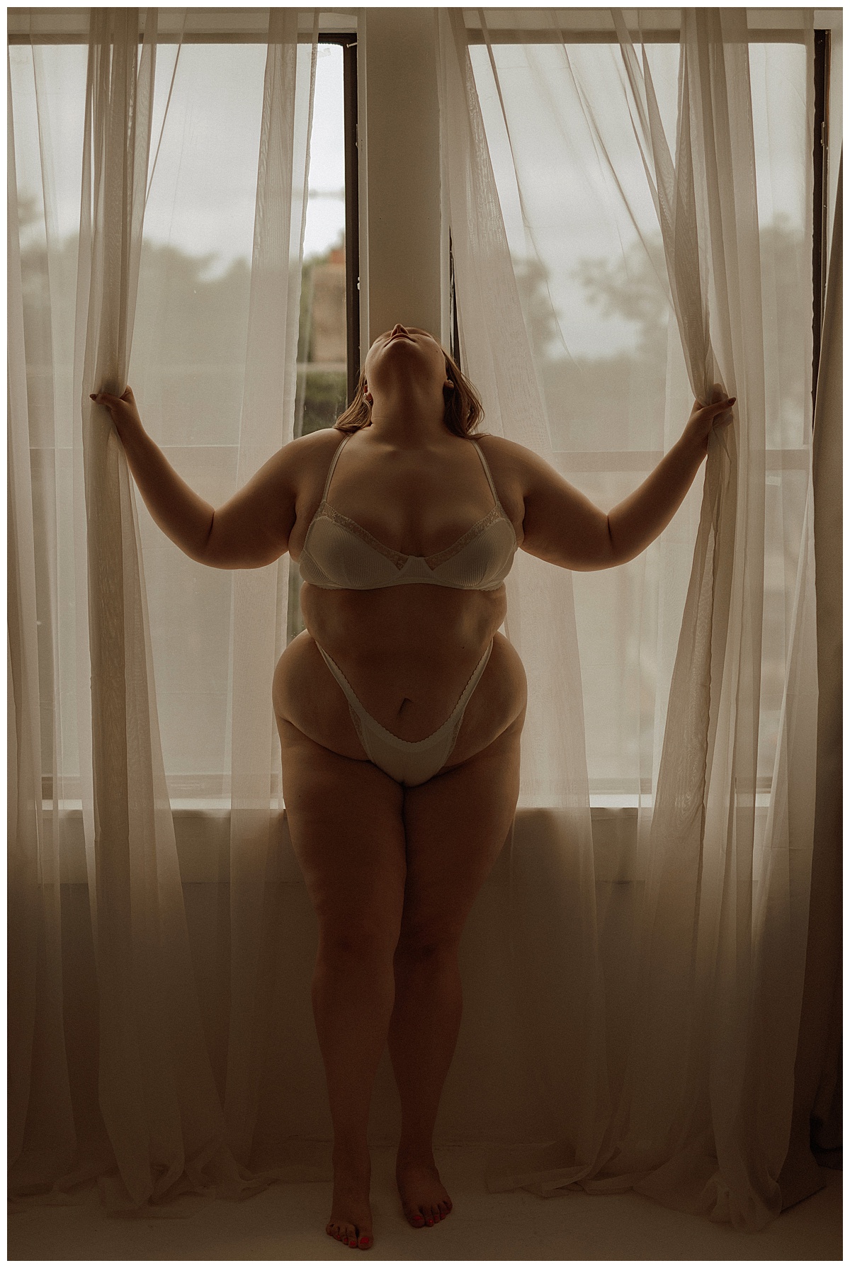 Adult pulls at window shades for Minneapolis Boudoir Photographer