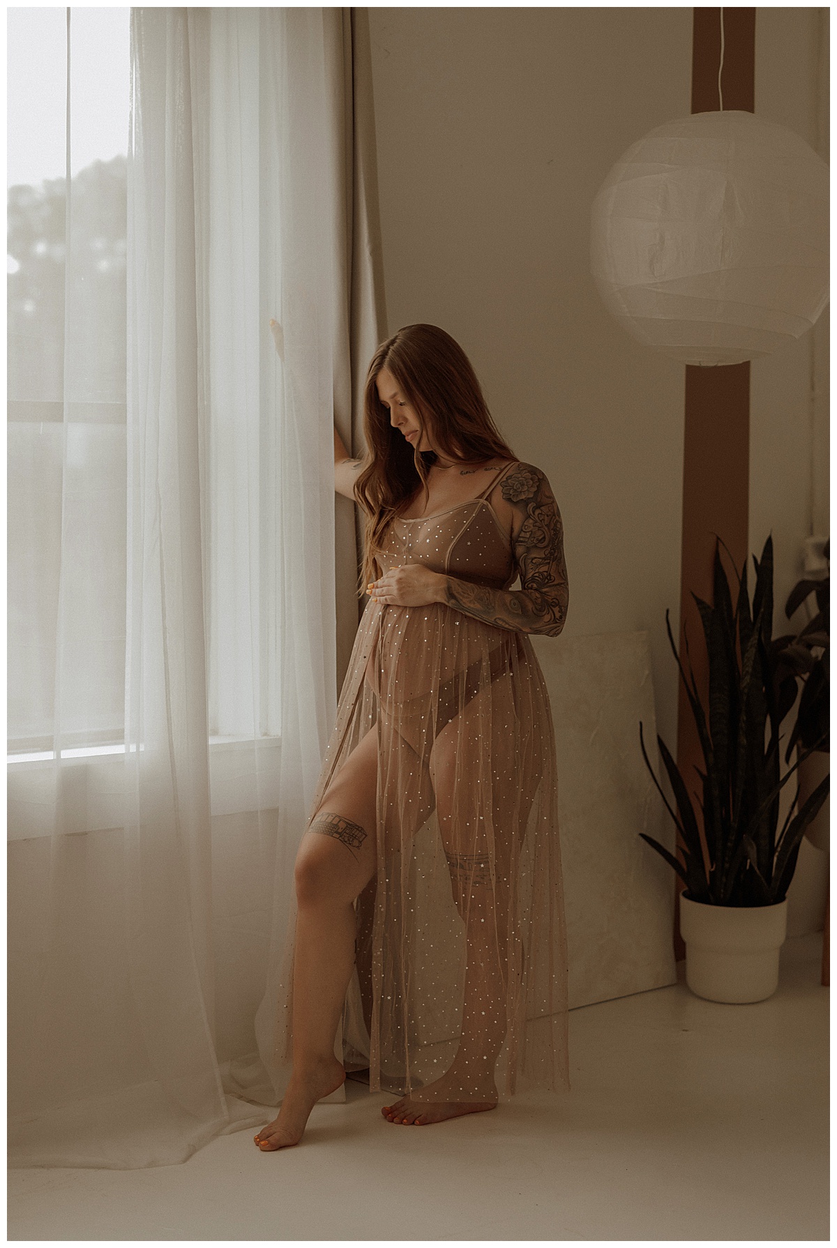 Female stands in front of the window showing What to Wear for Your Maternity Boudoir Photos