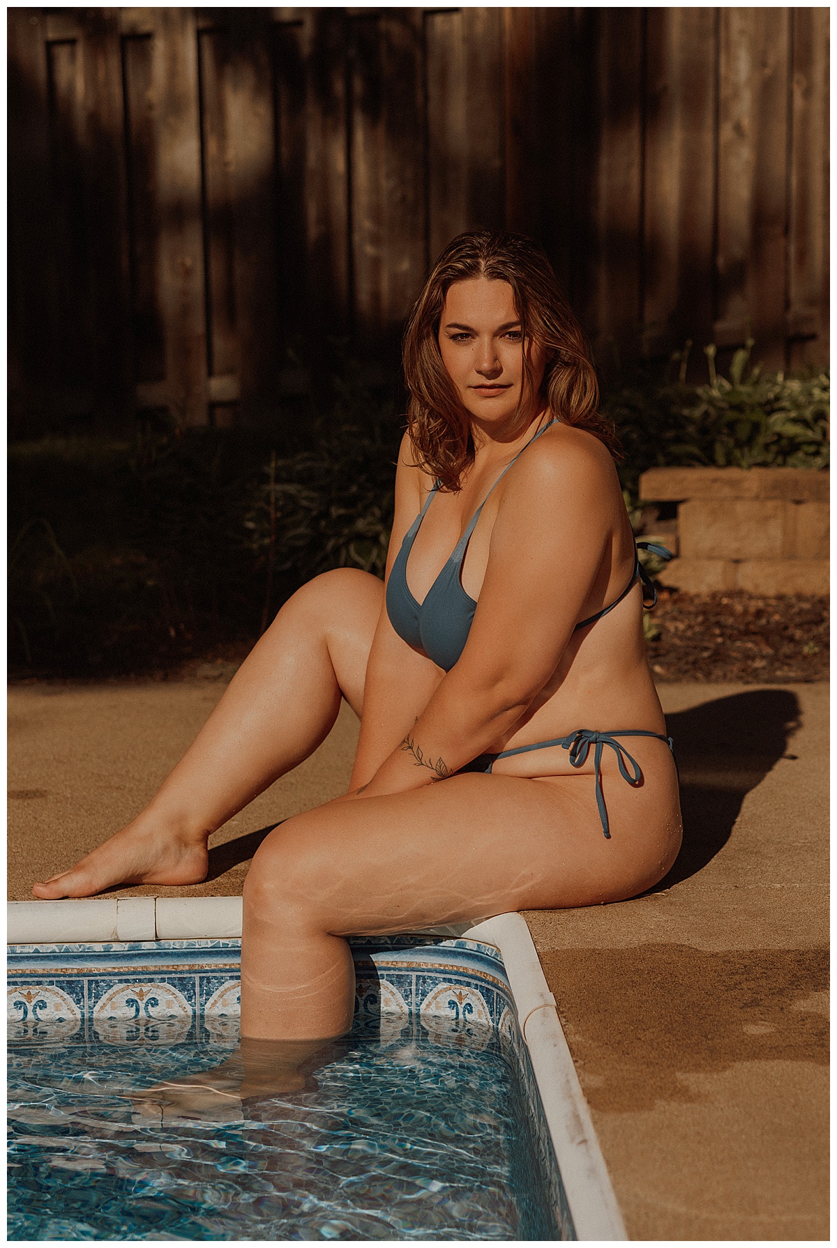 Adult sits on the pool edge wearing a blue swimsuit for Mary Castillo Photography