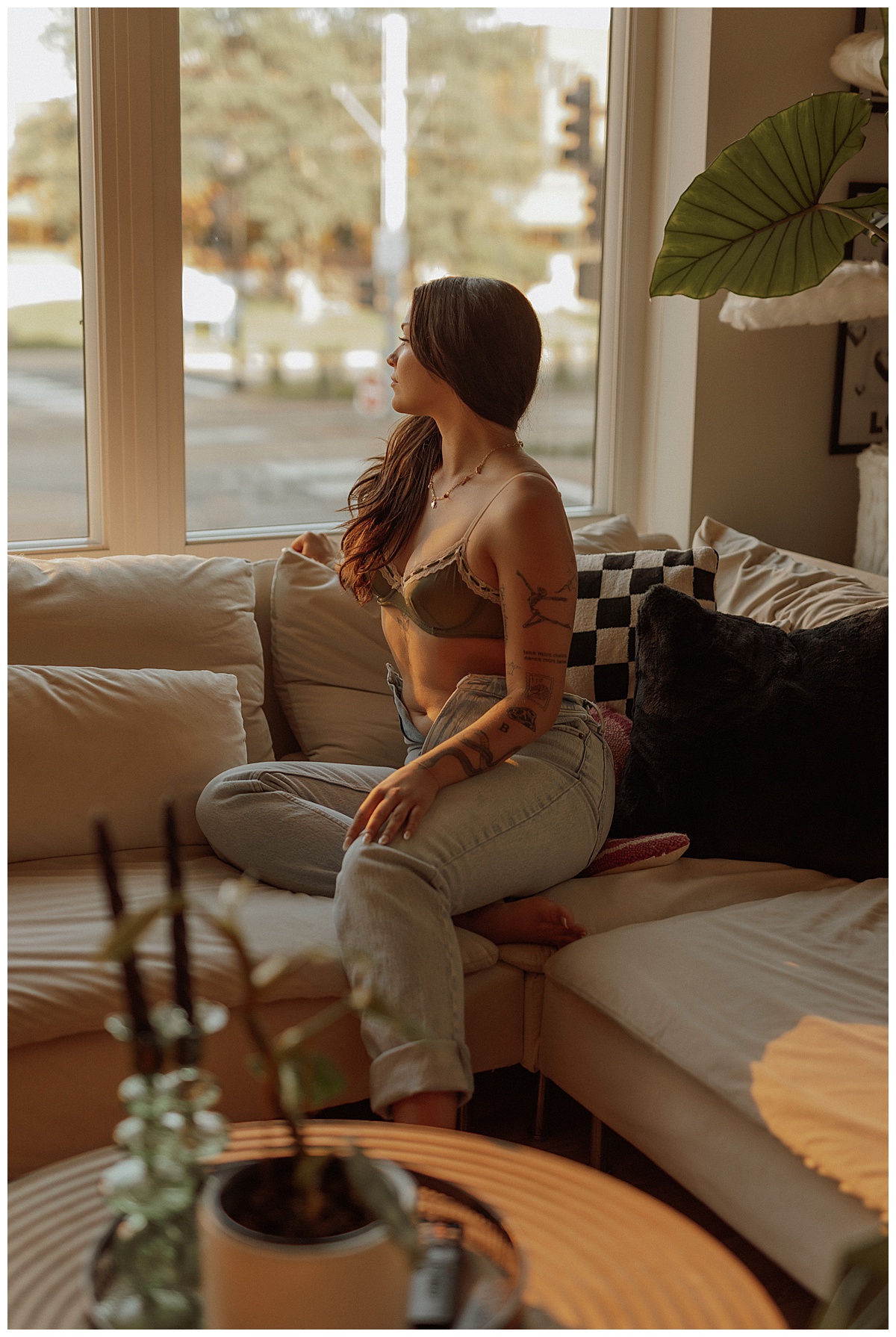 Person with tattoos sitting on couch in denim and bralette for creative session 