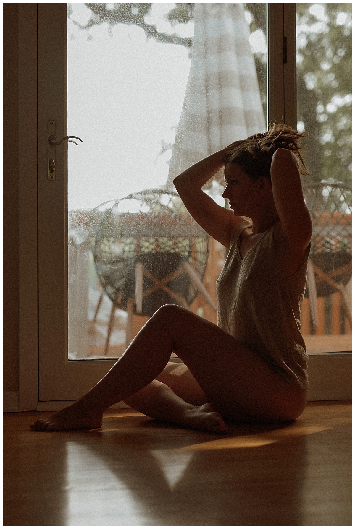 Lady holding hair in front of a window in tank by Minneapolis boudoir photographer