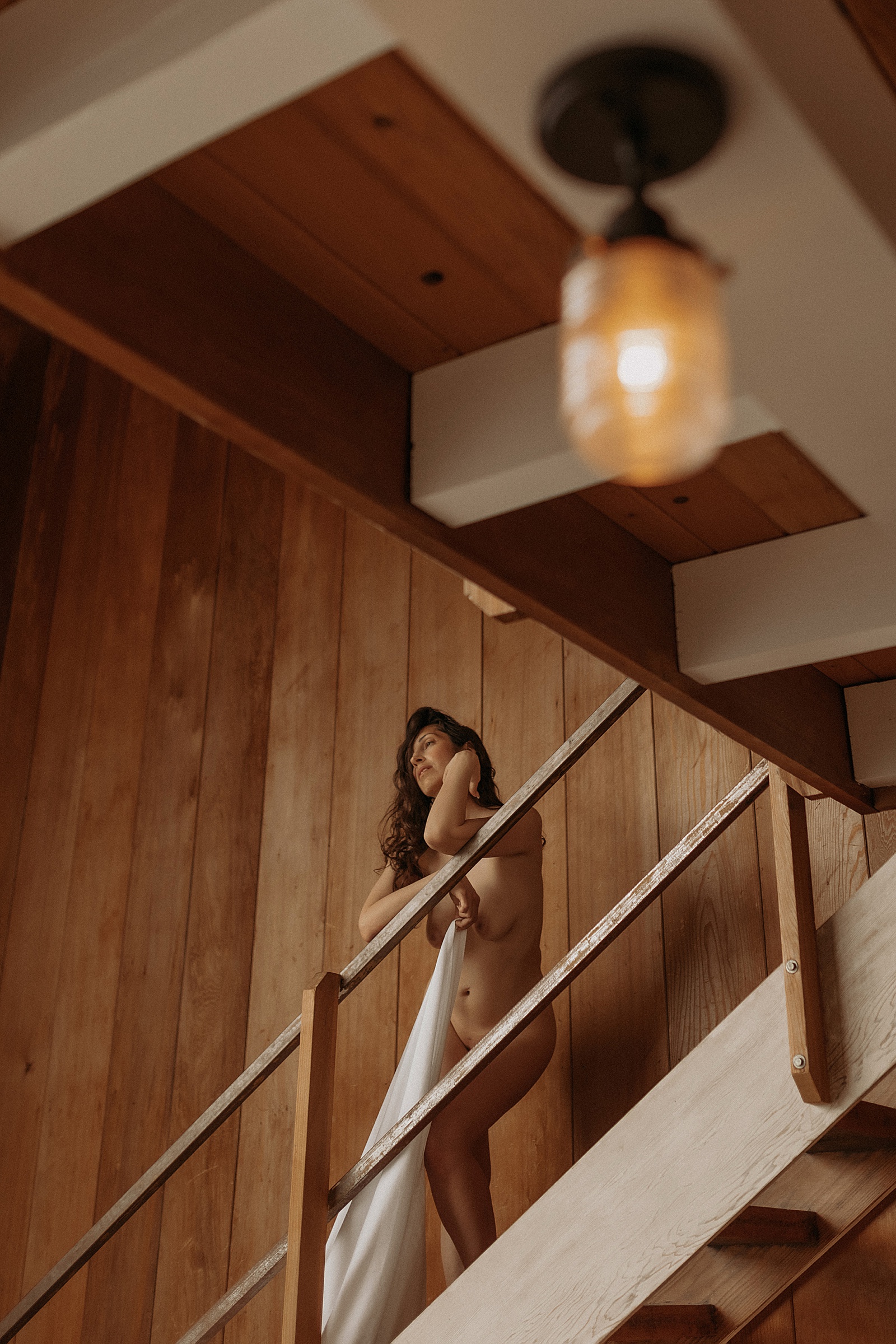 nude woman on staircase holding a sheet by Minneapolis boudoir photographer