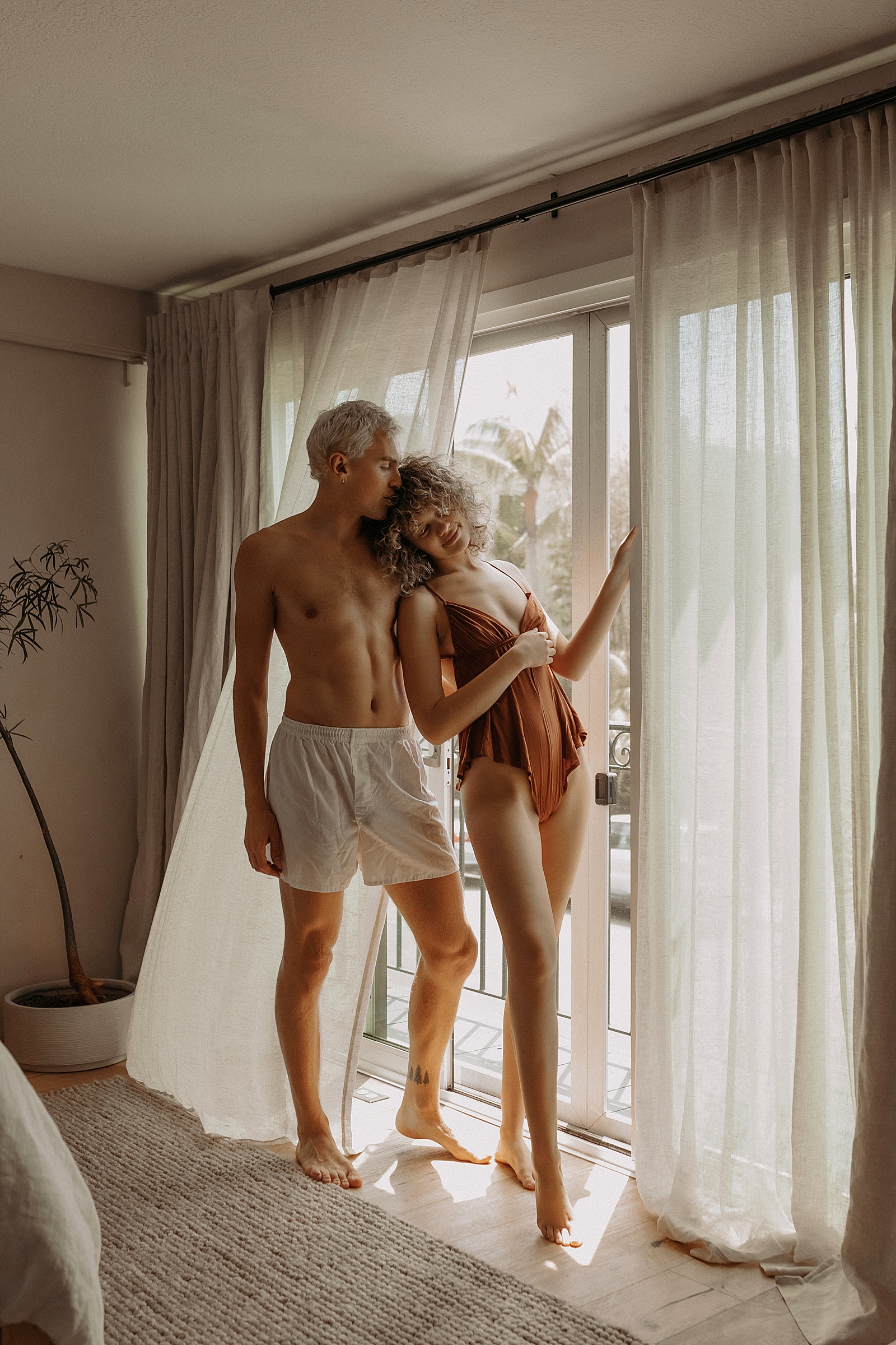 a couple in lingerie leaning next to a window by Mary Castillo Photography