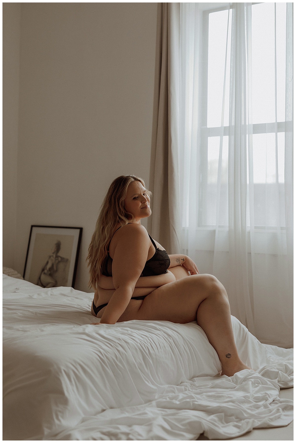 A woman sits on the bed wearing black lingerie set showing why You Deserve This boudoir session