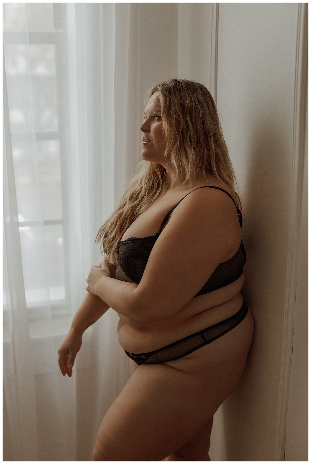 Adult stands against a wall wearing a black lingerie set for Mary Castillo Photography
