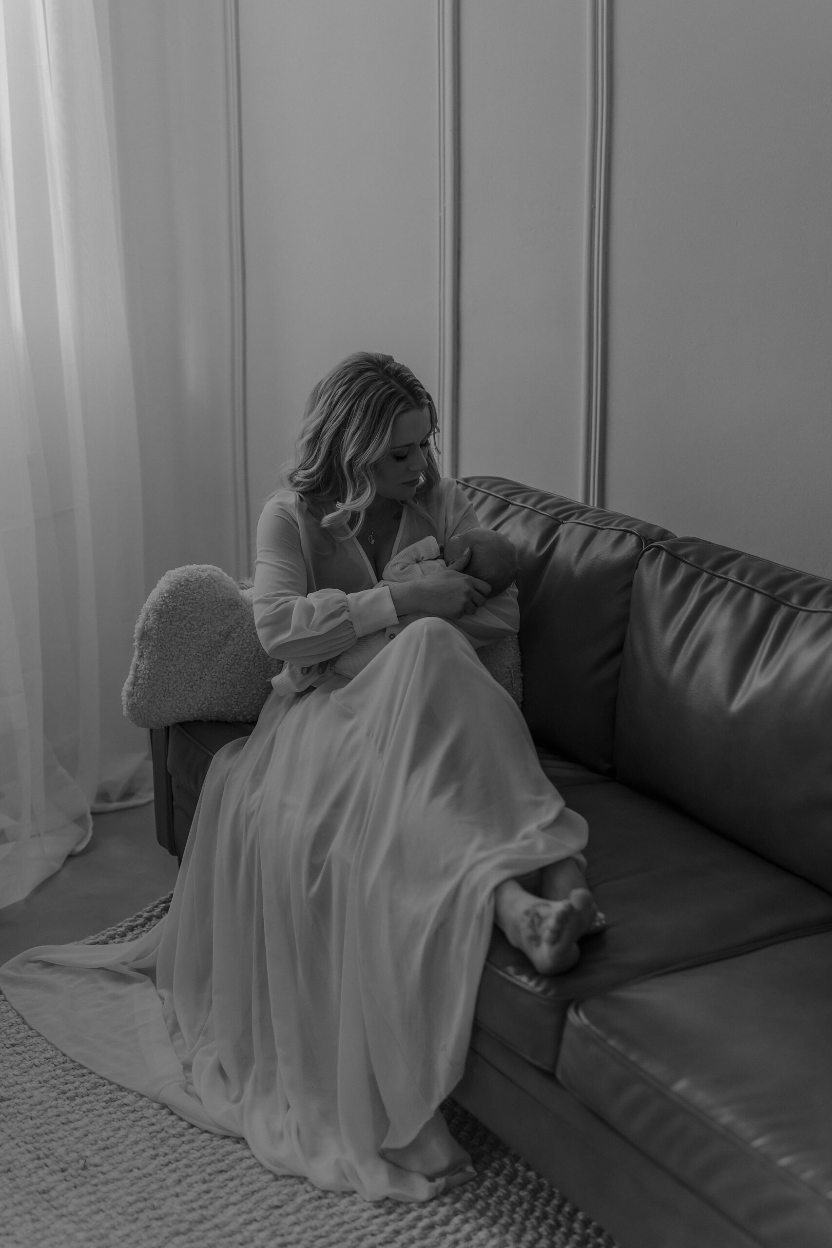 Black and white photo of mom with flowy dress cuddling baby on couch with Mary Castillo Photography