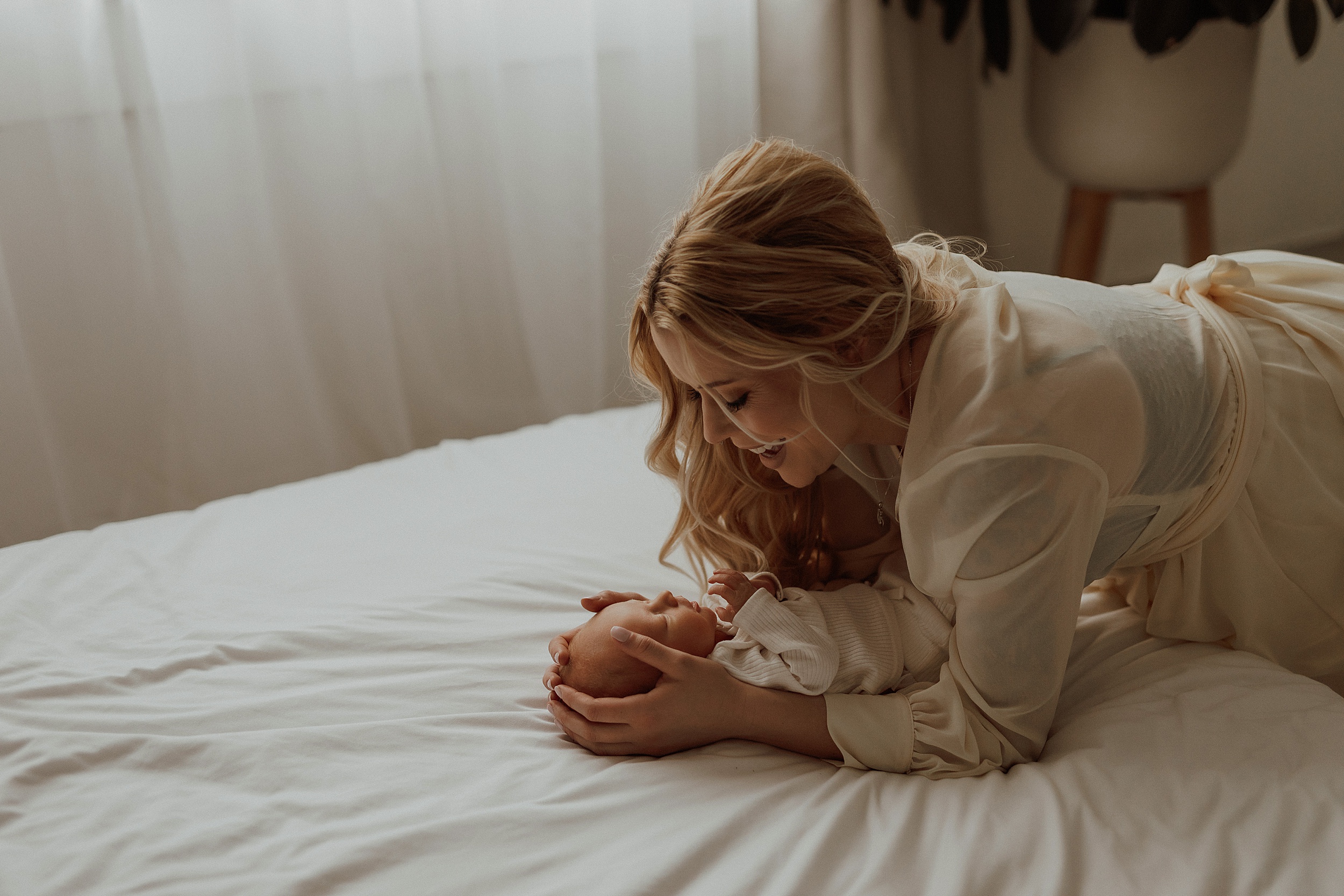 Mom kneels on bed to cradle baby at intimate newborn session