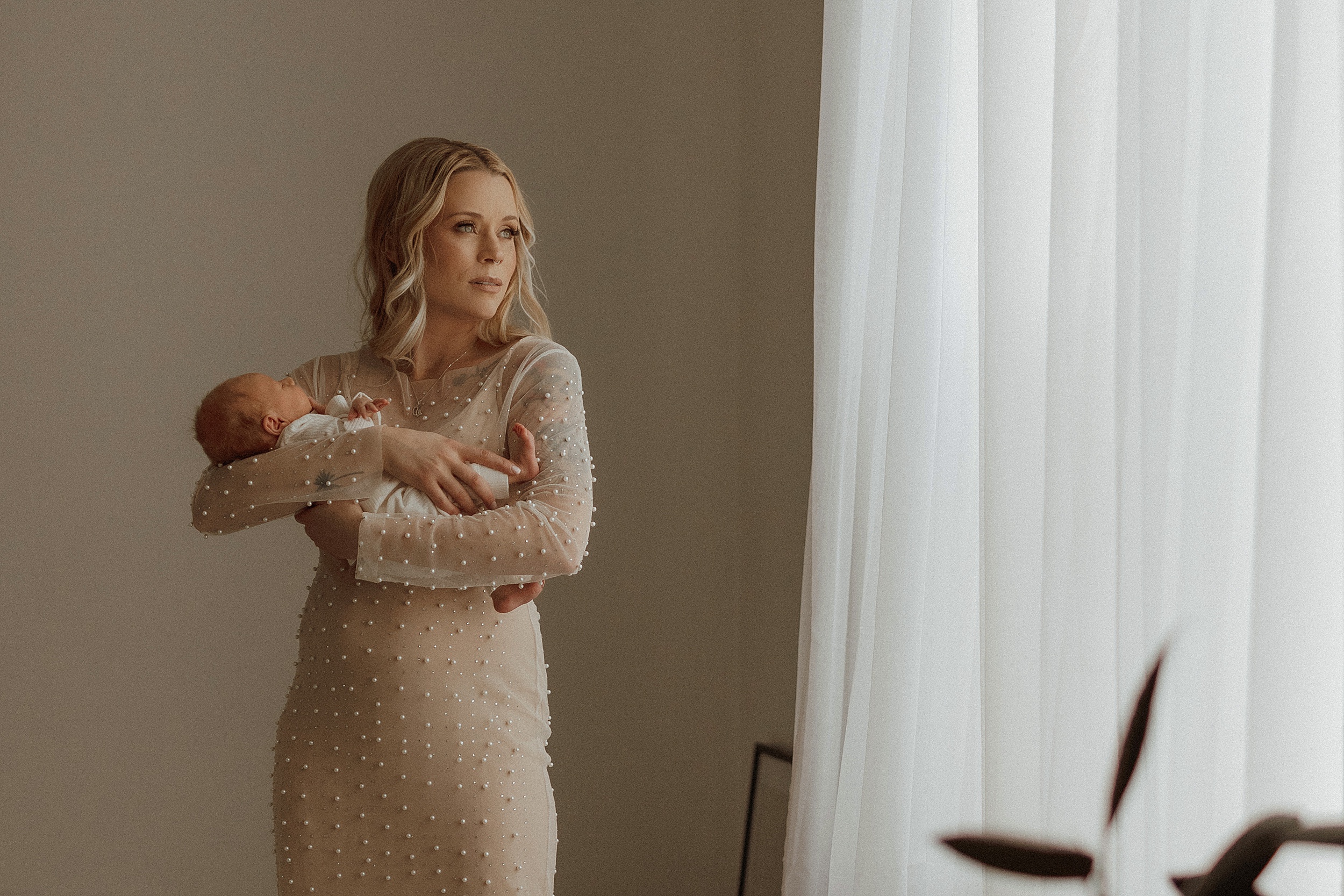 Wide shot of mother in embellished nude dress holding her newborn at Minneapolis Boudoir Photographer studio