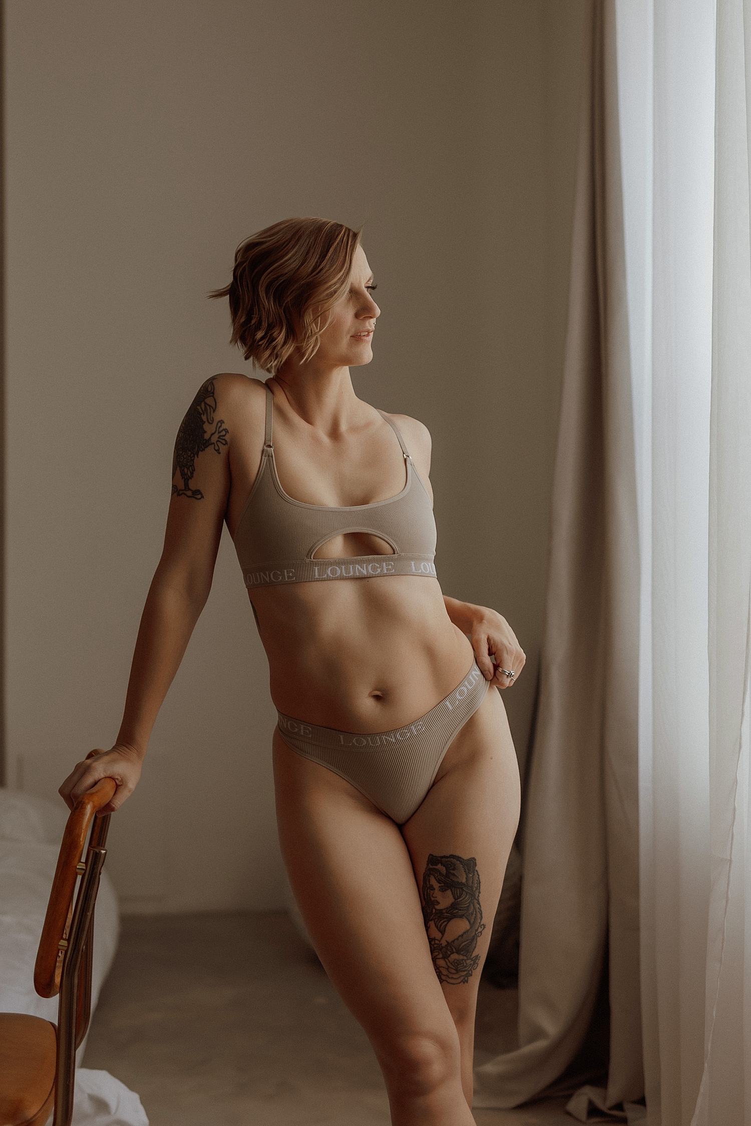 blonde stands next to window in lounge lingerie by Mary Castillo Photography