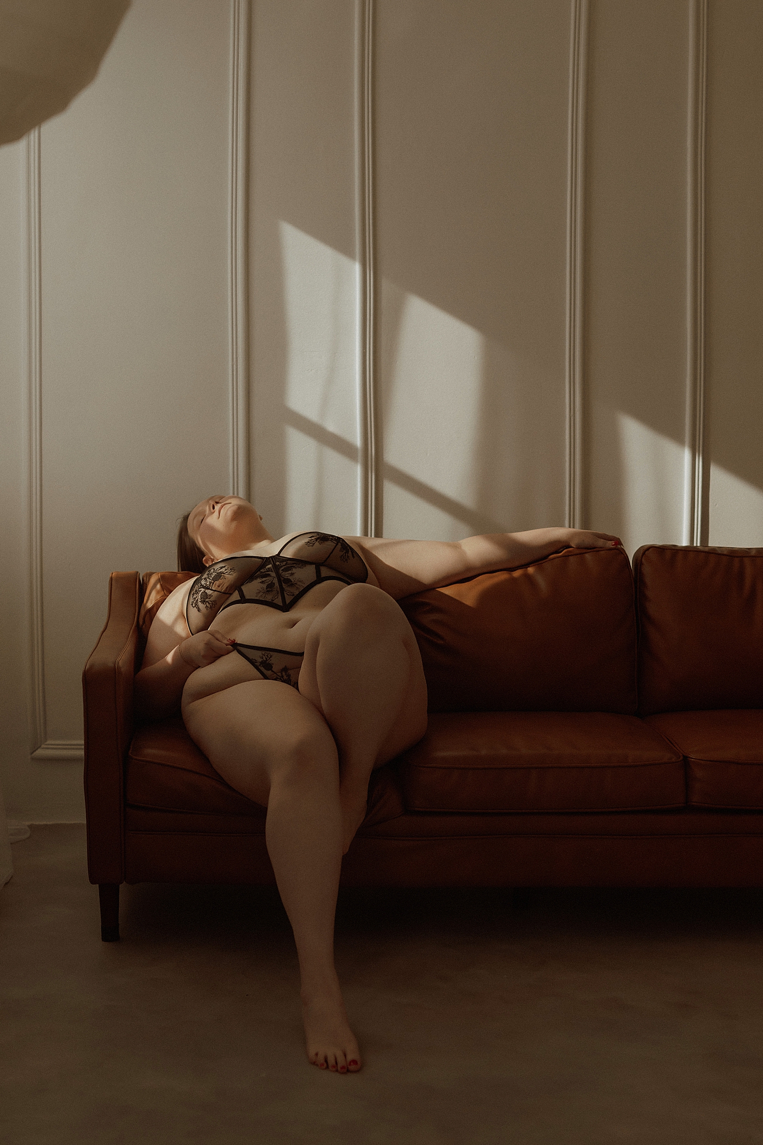 curvy model leans back against couch by Minneapolis boudoir photographer
