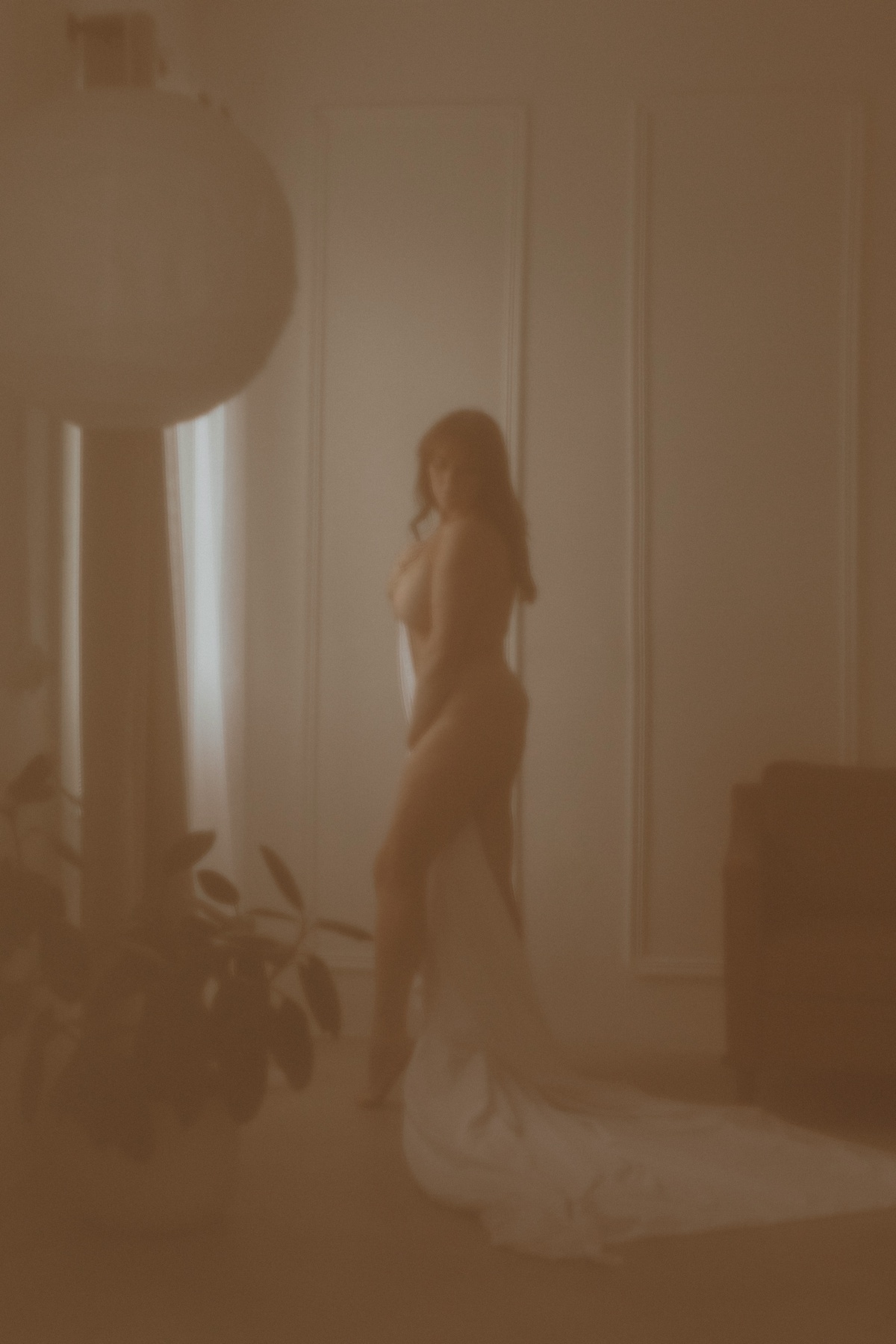 Woman standing against white wall holding a sheet to her body by Mary Castillo Photography