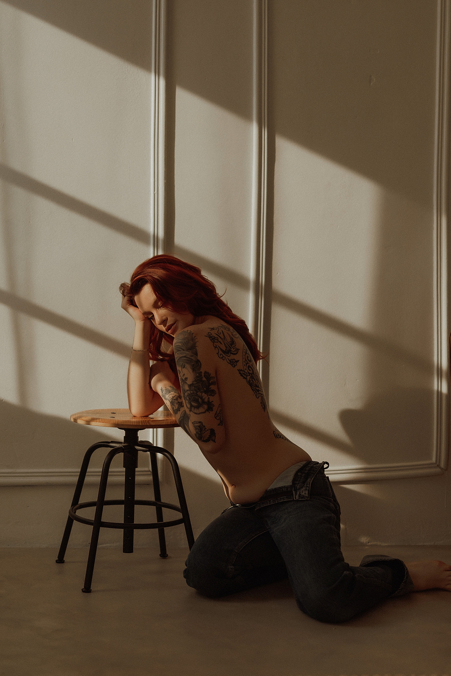 person with tattoos kneels topless over a stool by Mary Castillo Photography