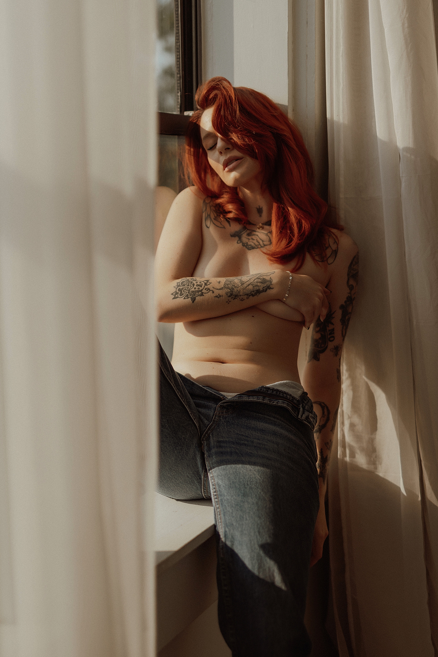 topless redhead sits in window surrounded by curtains for Golden Hour Model Session
