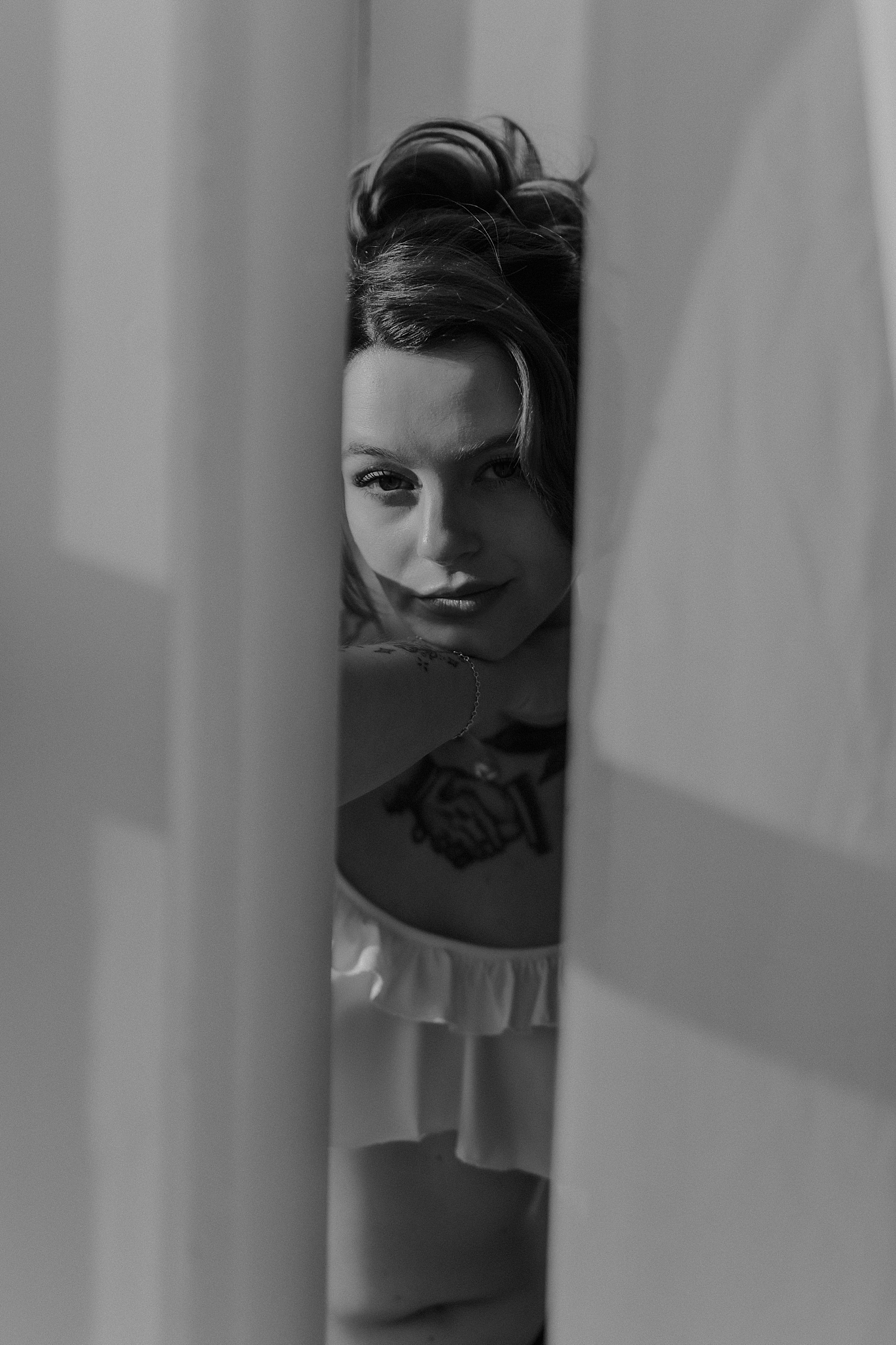 woman looks through curtains near window by Minneapolis boudoir photographer