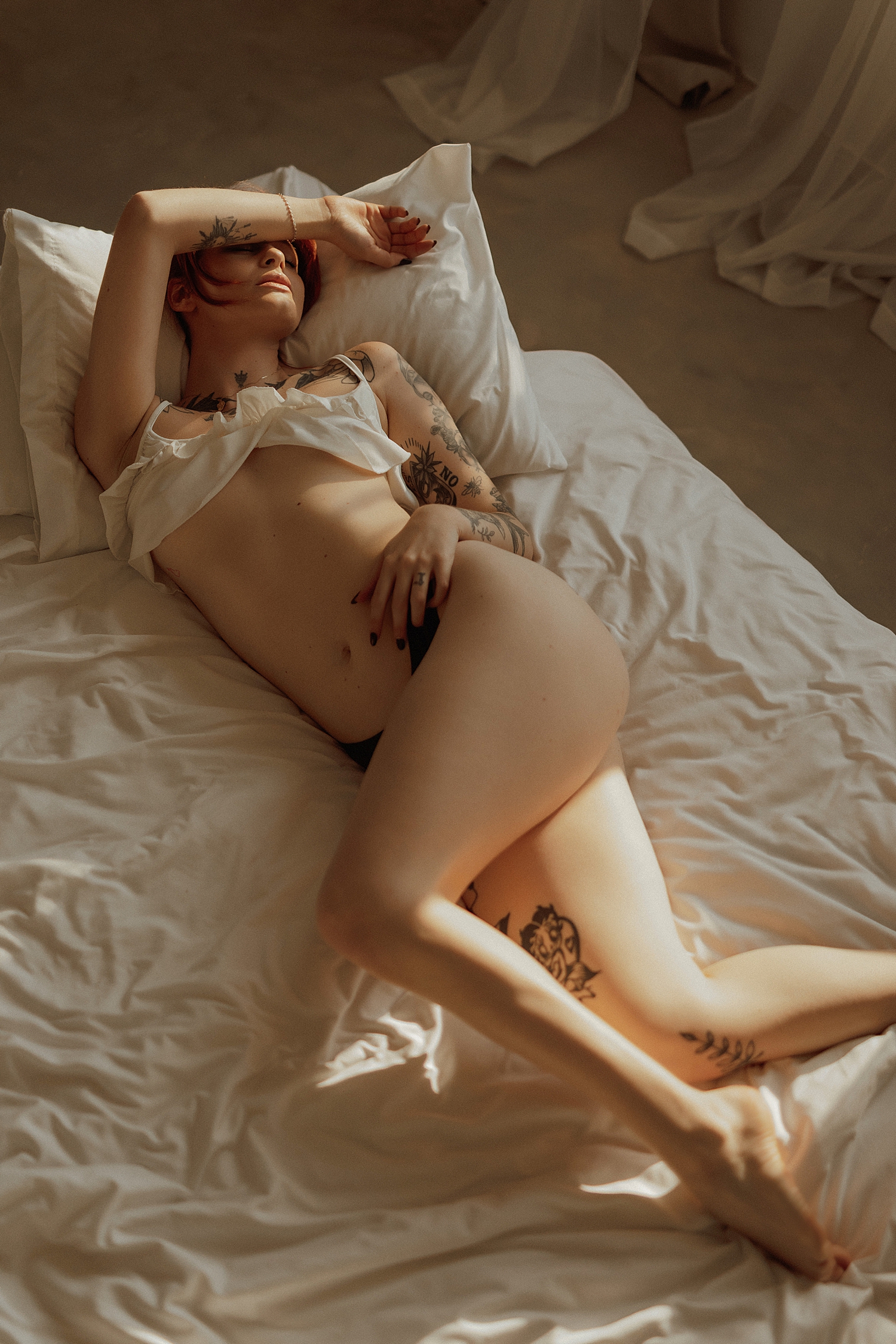 person lies across white bed in ruffle top and thong by Minneapolis boudoir photographer