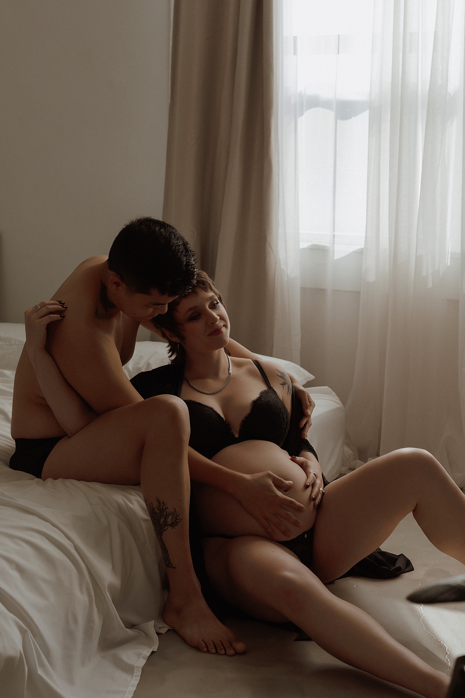 man and woman sit on mattress on floor for couples maternity session