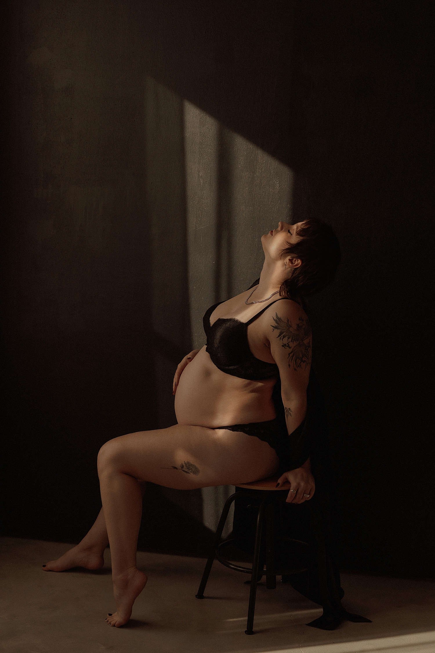 pregnant woman leans back on stool in studio by Minneapolis boudoir photographer