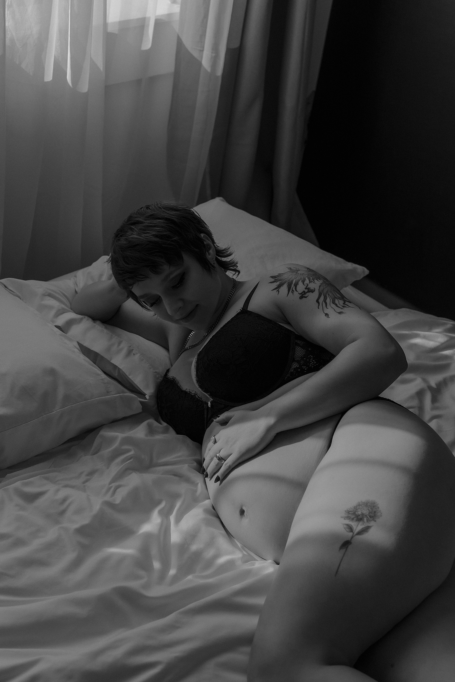woman with tattoos lies on bed holding her pregnant belly by Mary Castillo Photography