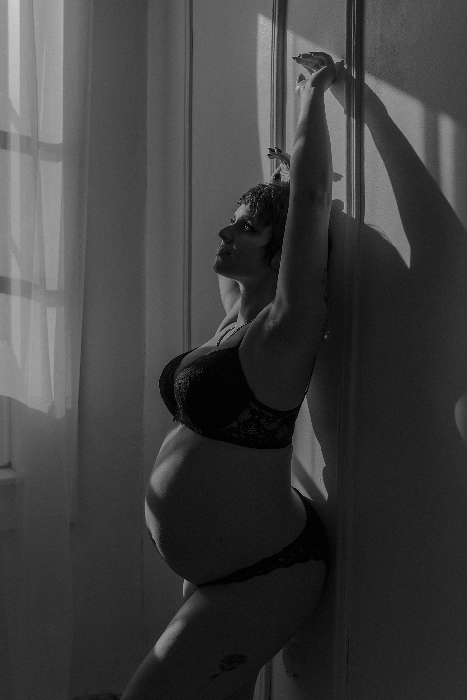 expecting mama leans back against studio wall for couples maternity session