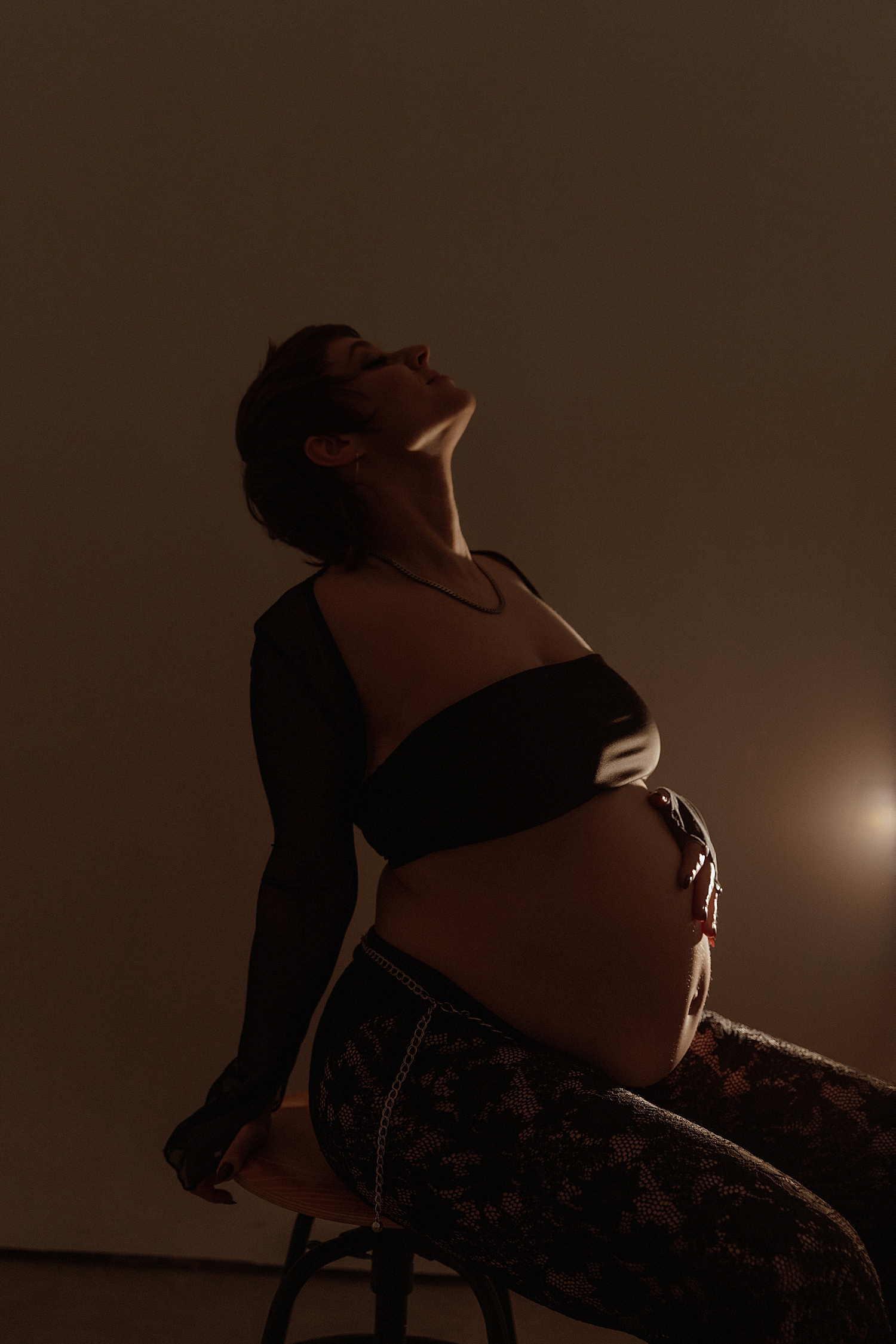 mother holds her bump as she arches her neck back by Minneapolis boudoir photographer
