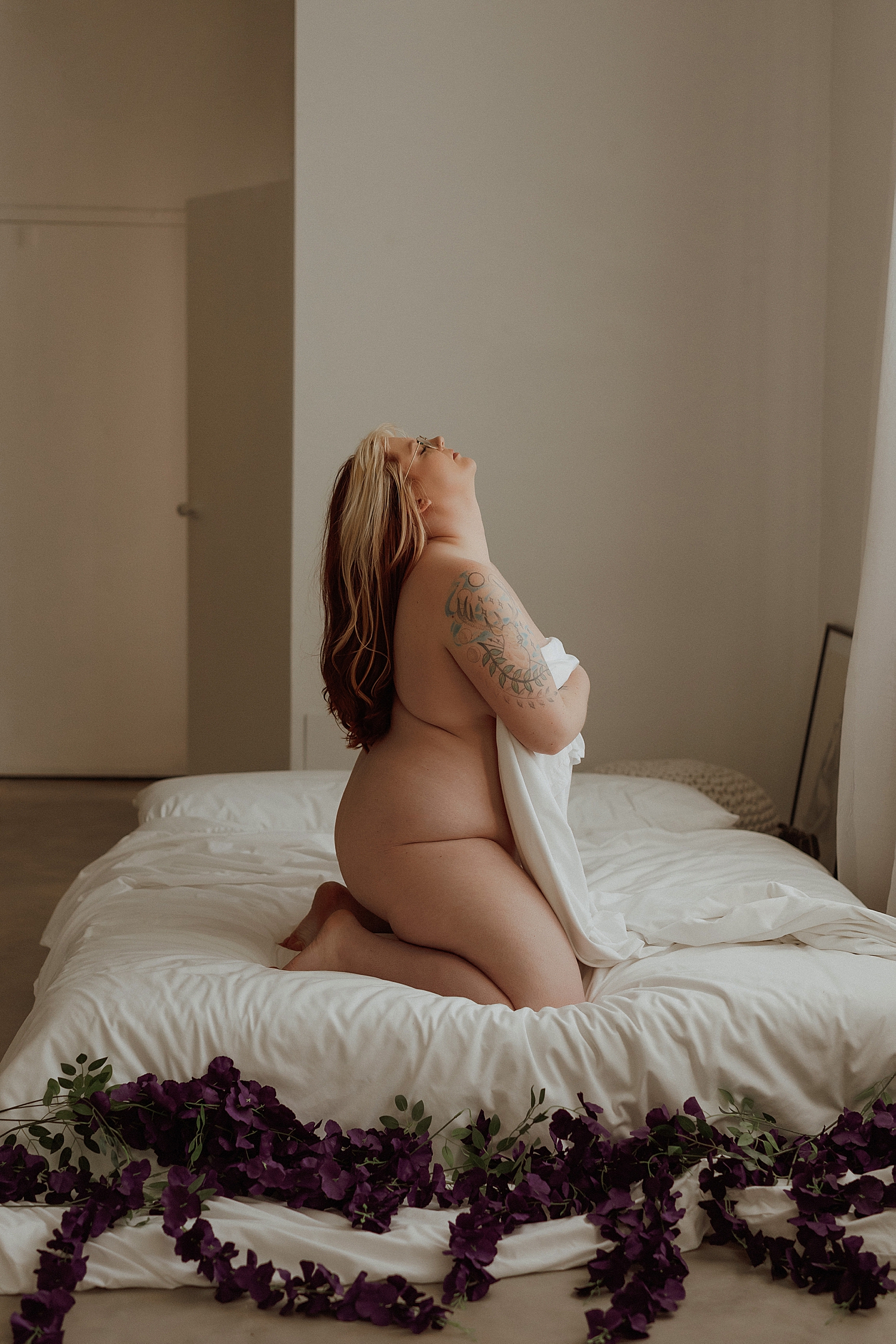 person with tattoos kneels on mattress and covers with sheet by Mary Castillo Photography